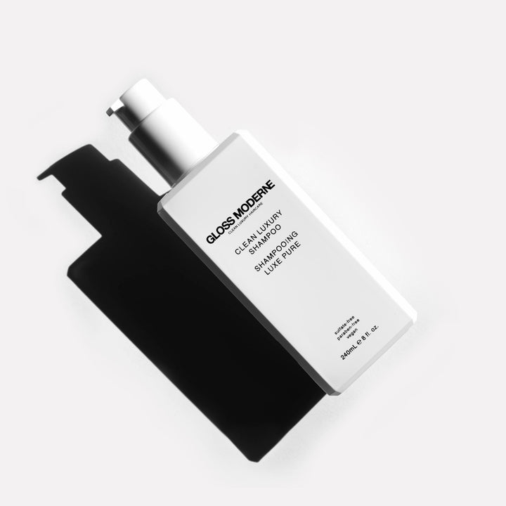 white bottle of clean luxury shampoo on a white surface with strong shadows